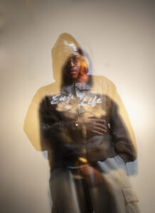mo beanie stands with his hand on his chest, captured with an after-effect and artistic light treatment.
